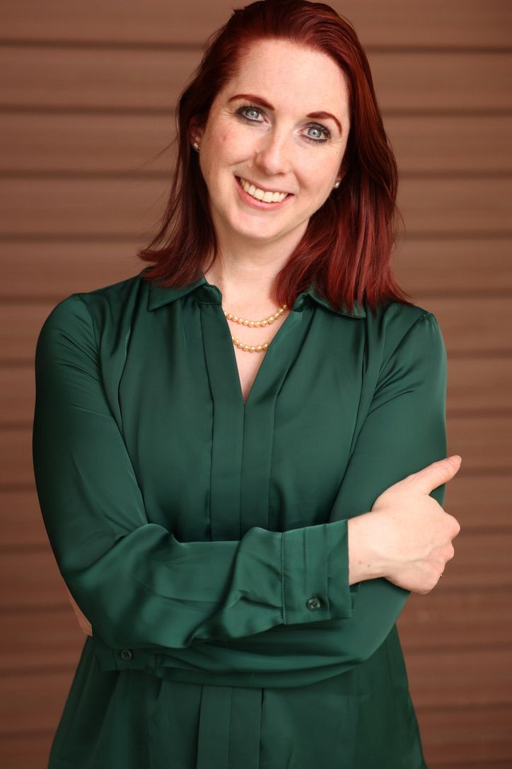 Person wearing a dark green shirt with arms crossed, adorned with a pearl necklace.